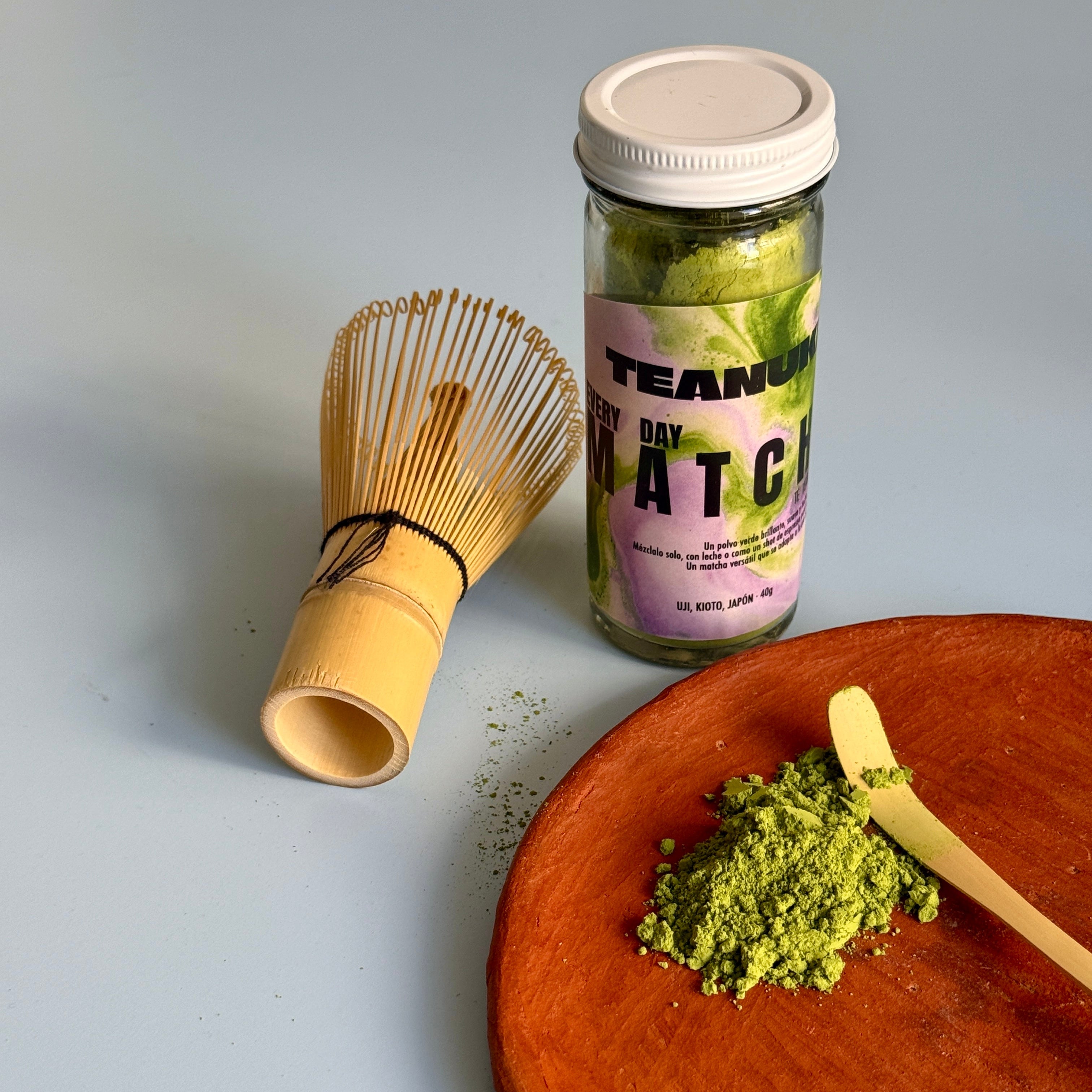 Everyday Matcha green tea powder from Teanuki with a bamboo whisk and a container on a light blue background