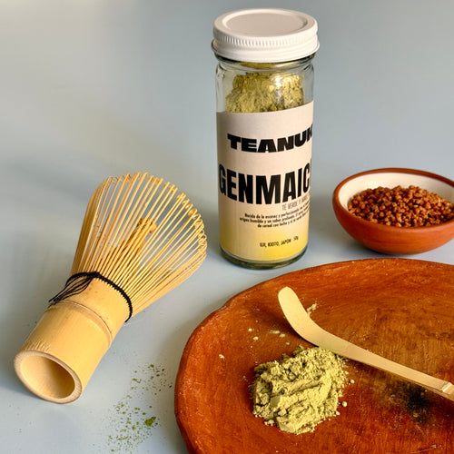 Tea packaging with a whisk and wooden spoon on a plate with green tea powder, on a light gray background.