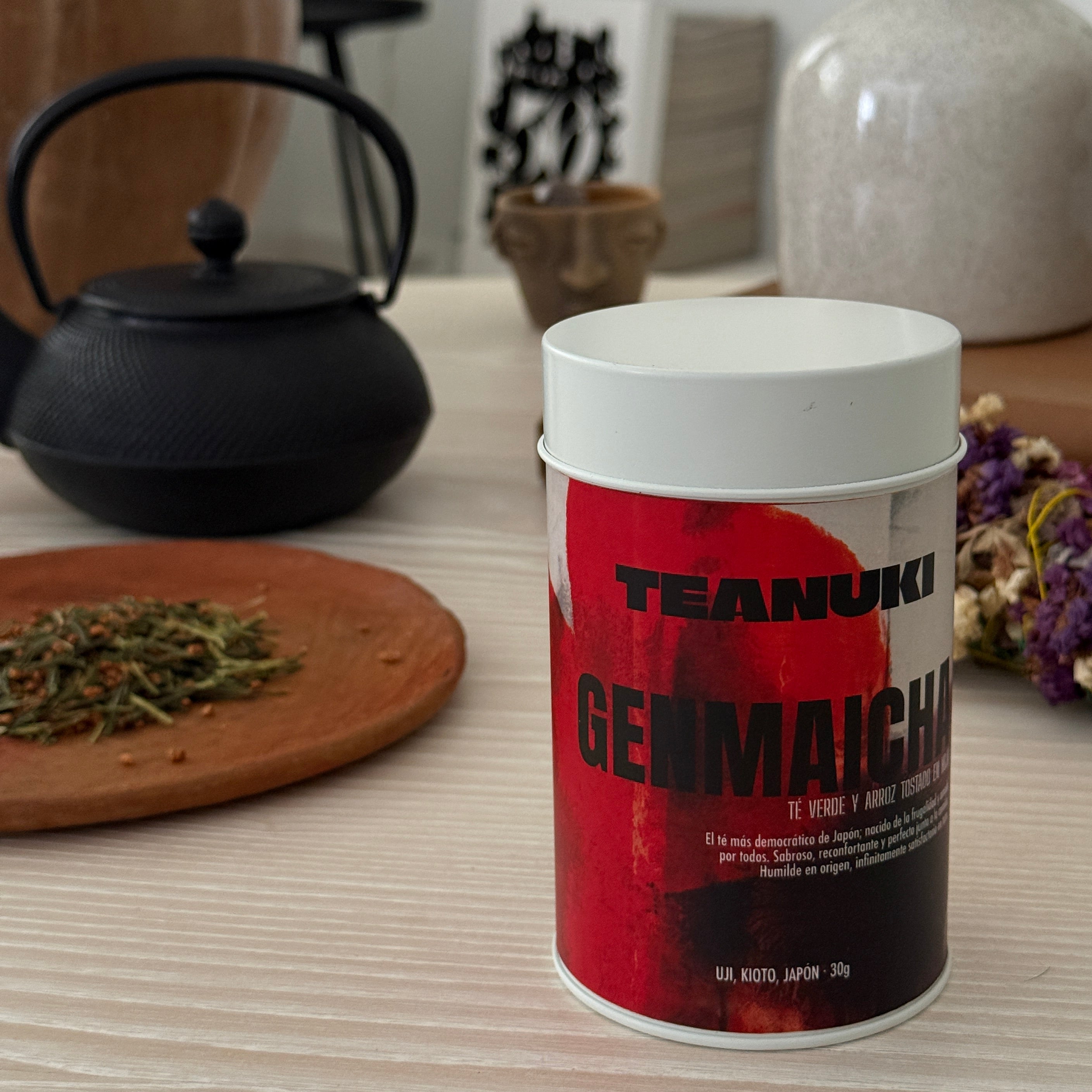 Red and white tea container with text Teanuki Genmaicha on a coffee table with tea-making setup. 