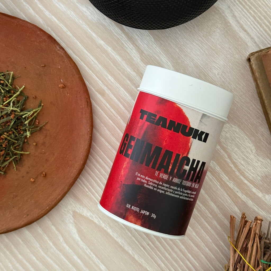 Teanuki genmaicha green tea tin packaging with a red label on a wooden surface with herbs and a black lid.