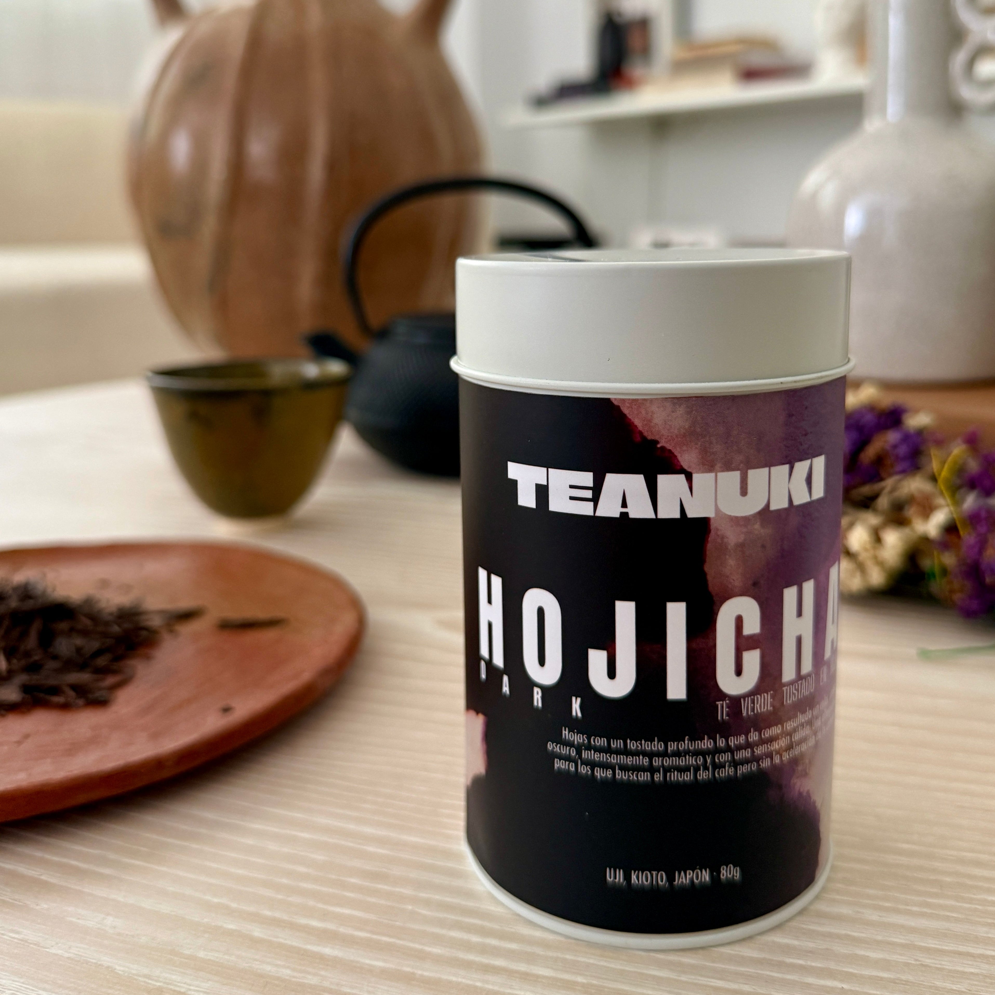 Teanuki Hojicha dark roast tea canister on a table with decorative items in the background