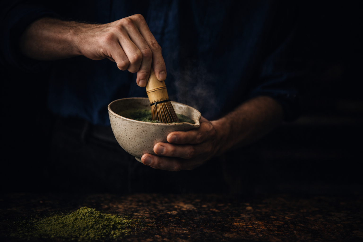 Person preparing matcha tea with a whisk in a dark setting